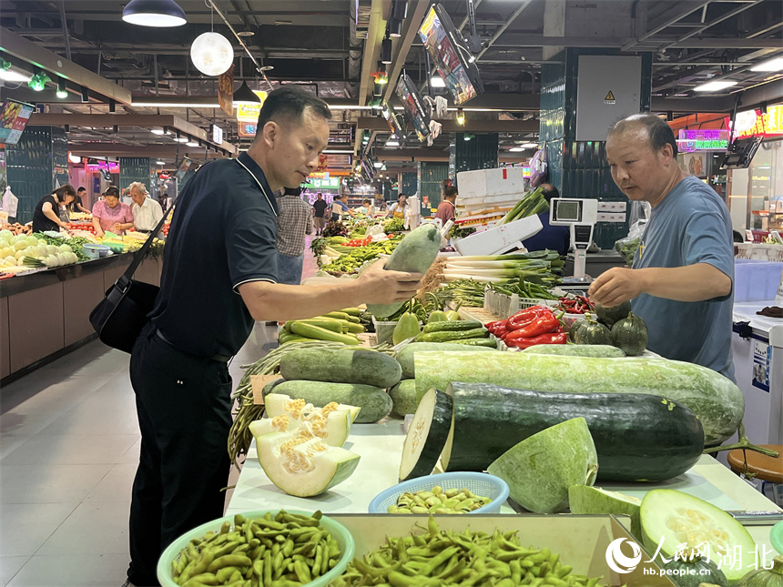 晚高峰時段，一名背著公文包的男士路過洪山廣場地鐵站菜市場買菜。人民網(wǎng)記者 張雋攝