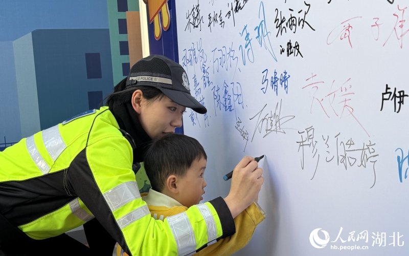 歲的小男孩在交警小姐姐帶領(lǐng)下，在文明禮讓承諾墻簽下自己的大名。人民網(wǎng)記者 周恬攝